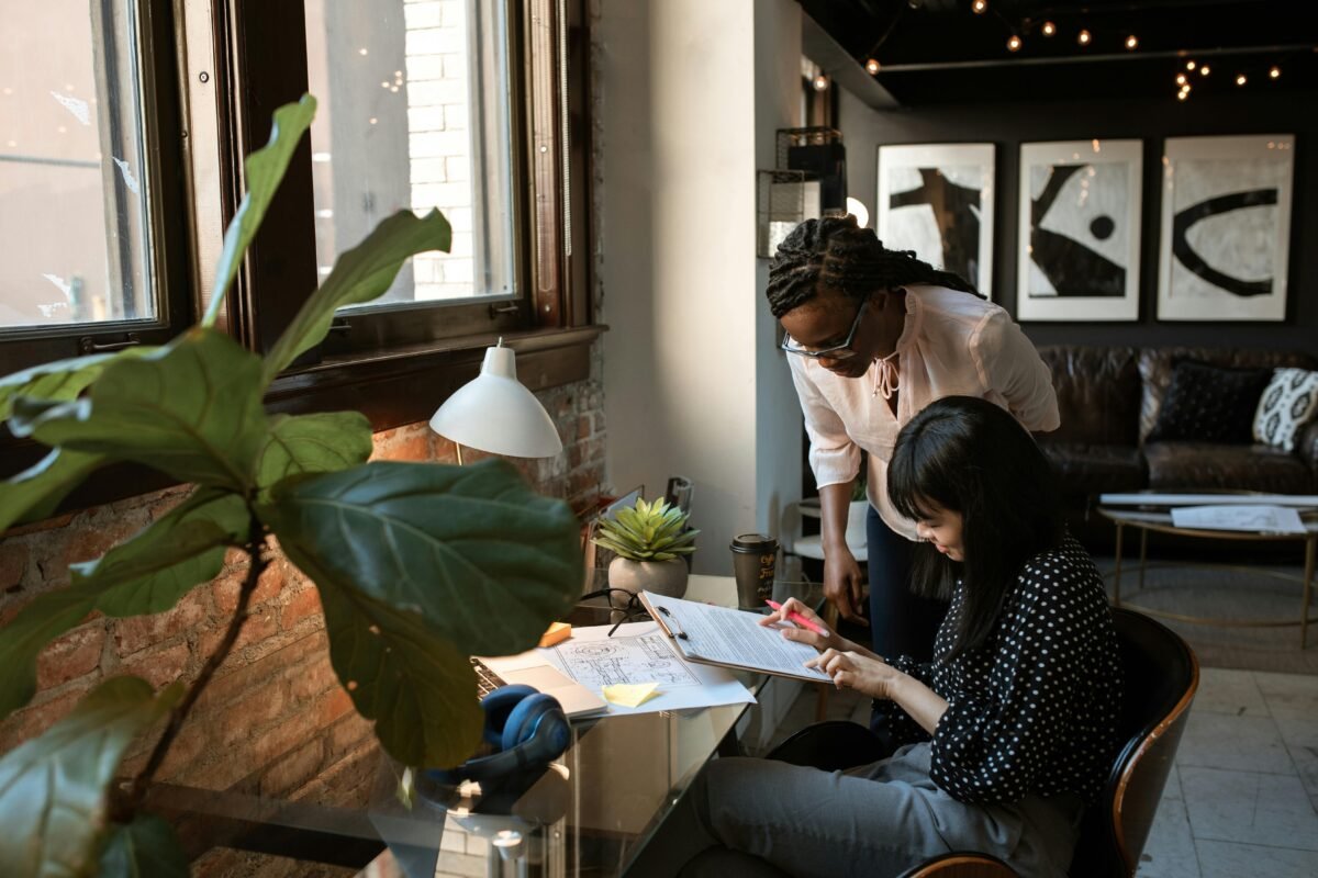 Two professionals collaborating in a modern, stylish workspace with natural light and greenery, representing teamwork and creativity.