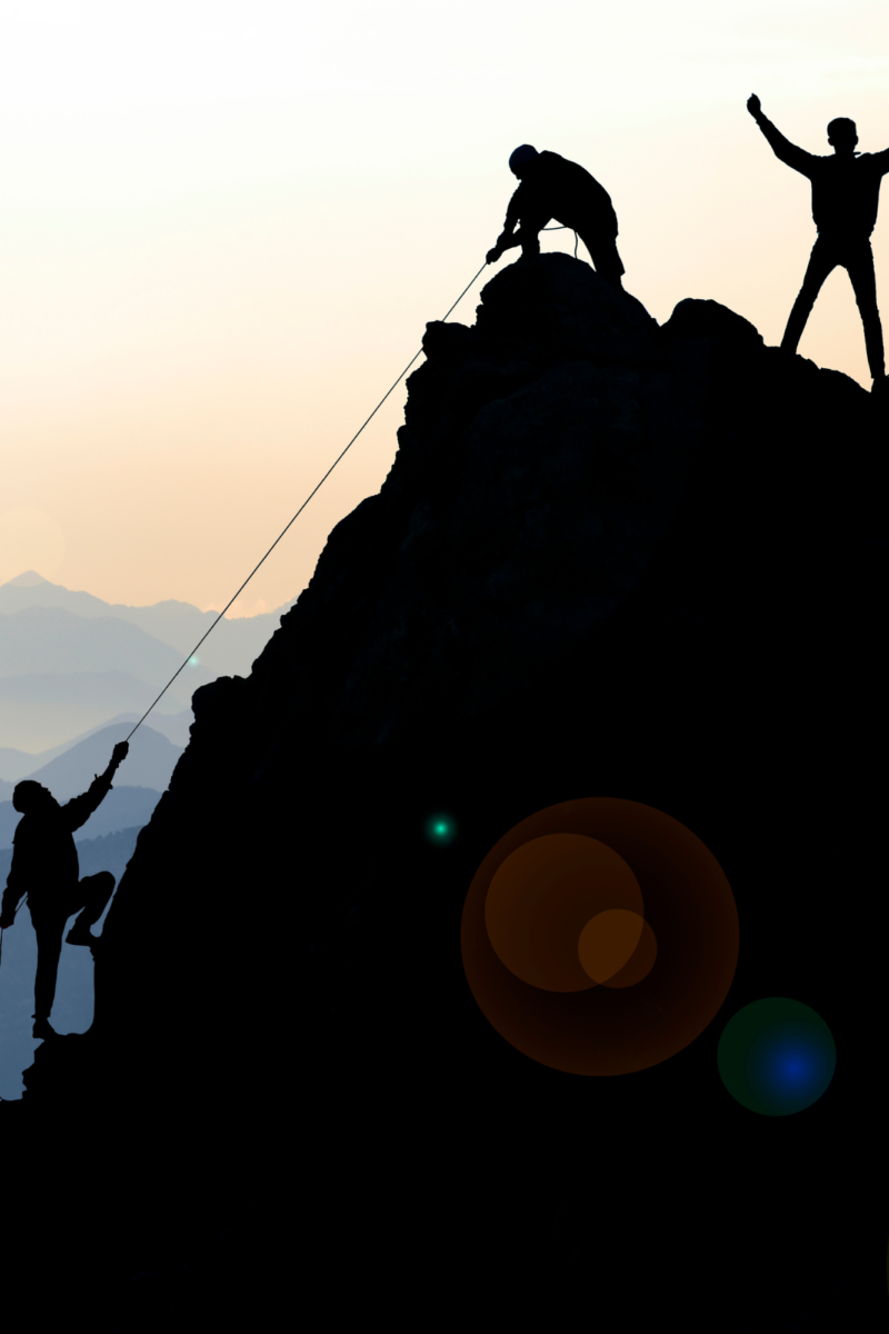 Silhouettes of climbers scaling a rocky mountain at sunrise, with one person reaching the peak and celebrating, symbolizing teamwork, perseverance, and achieving success against challenges.