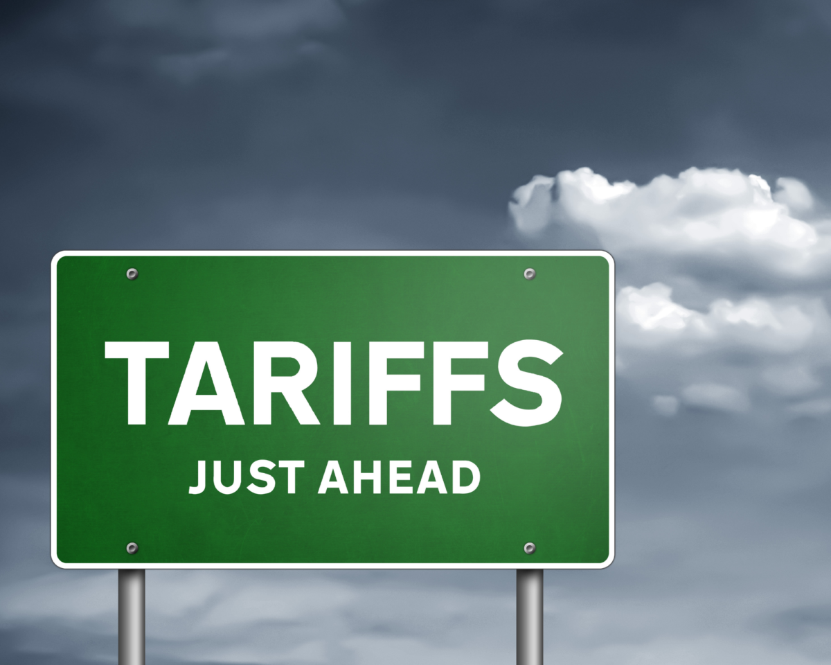 A green road sign with bold white text reading "TARIFFS JUST AHEAD" against a cloudy sky. This image represents upcoming trade changes and the need for businesses to navigate the tariff effect effectively.